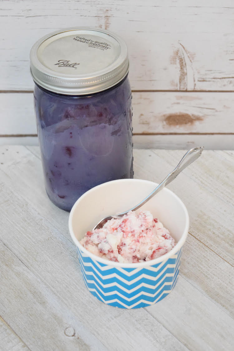 homemade strawberry ice cream in a chevron paper bowl in front of a purple mason jar filled with homemade ice cream