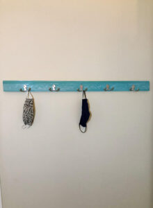 A DIY face mask rack made with double coat hooks, pretty chair rail molding, and spray painted a beautiful blue green