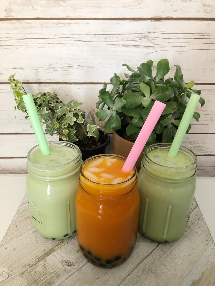 Matcha bubble (boba) teas in mason jars with iced. Behind them are a potted ivy plant and a succulent.