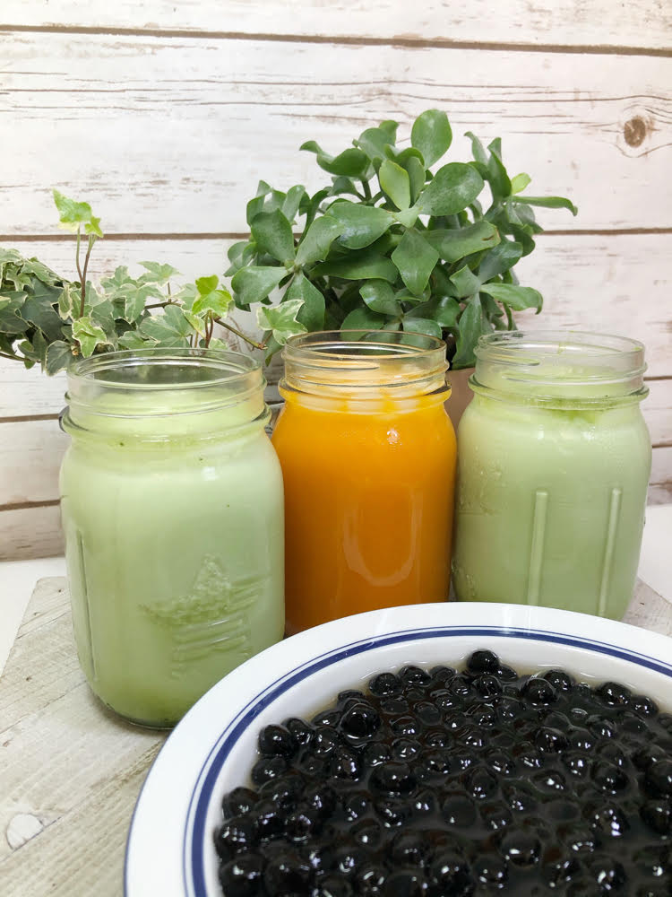 Iced matcha green tea and iced Thai tea in mason jars behind a bowl of cooked boba.