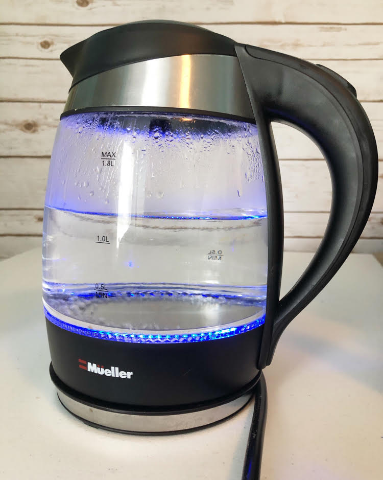 blue lit electric tea kettle filled with boiling water against a shiplap or plank wall