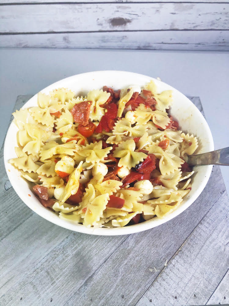 a bowl of pasta salad with roasted red peppers, salami and mozzarella pearls