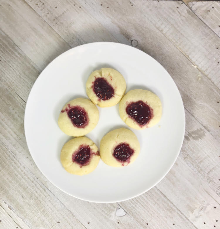 Raspberry shortbread thumbprint cookies on a white plate against a gray wood background