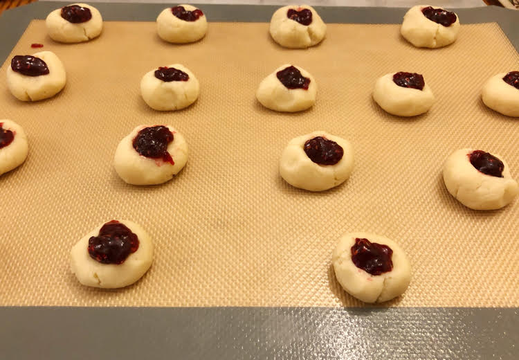 raspberry thumbprint cookies on a silicone backing mat on a baking sheet