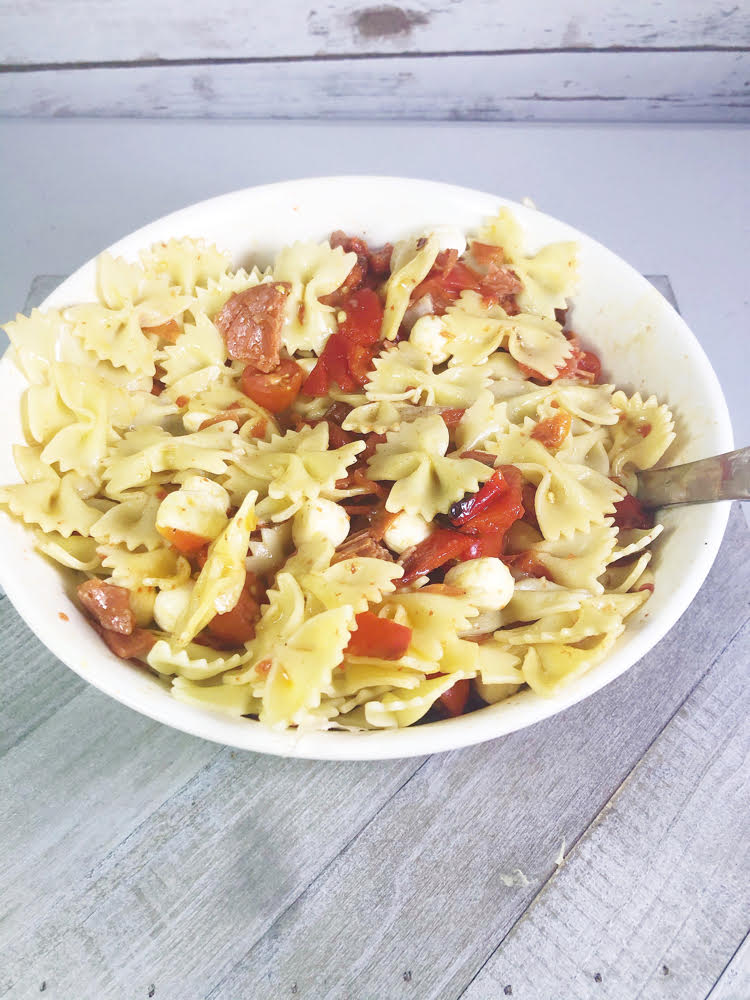 a bowl of pasta salad with mozzarella balls, roasted red pepper, cherry tomatoes, and homemade Italian dressing