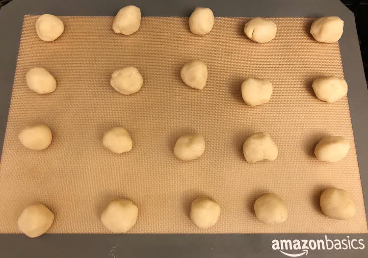 Balls of shortbread cookie dough on a silicone baking mat on a cookie sheet