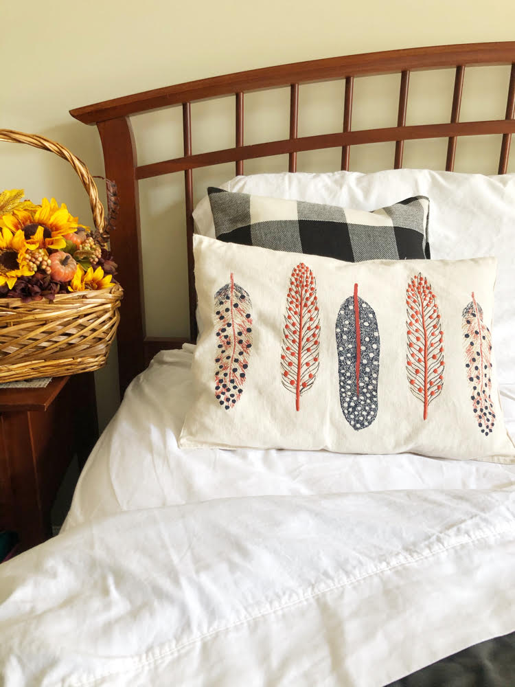 a bed decorated for fall with a basket with sunflowers on a nightstand, a plush blanket and fall pillows