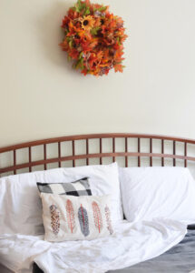 farmhouse style bed with a cozy gray plush Therapedic blanket, white sheets and a fall leaf wreath on the wall