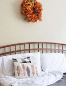 farmhouse style bed with a cozy gray plush Therapedic blanket, white sheets and a fall leaf wreath on the wall