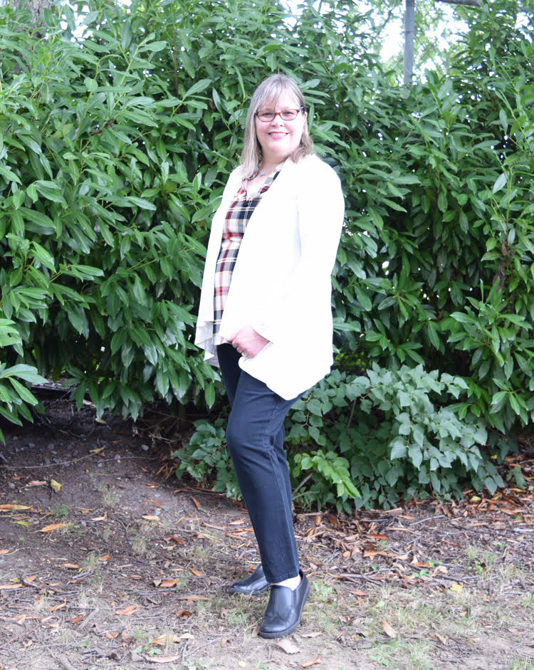 woman wearing a black, white and red plaid top, open white cardigan and dark wash jeans.