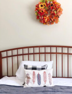 farmhouse style bed with slat headboard, a fall wreath on the wall and pretty fall pillows and a cozy gray blanket