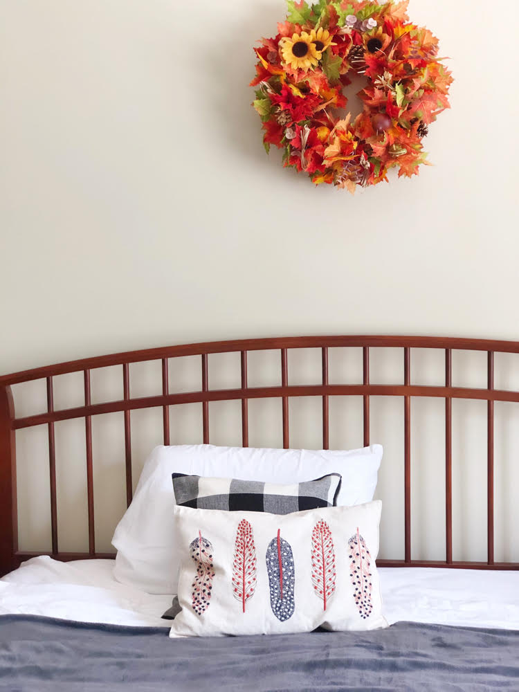 farmhouse style bed with slat headboard, a fall wreath on the wall and pretty fall pillows and a cozy gray blanket