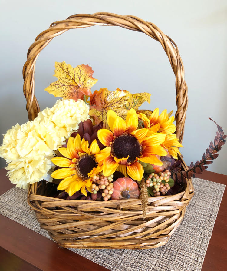 A faux floral arrangement in a basket with silk fall leaves, mini pumpkins and sunflowers