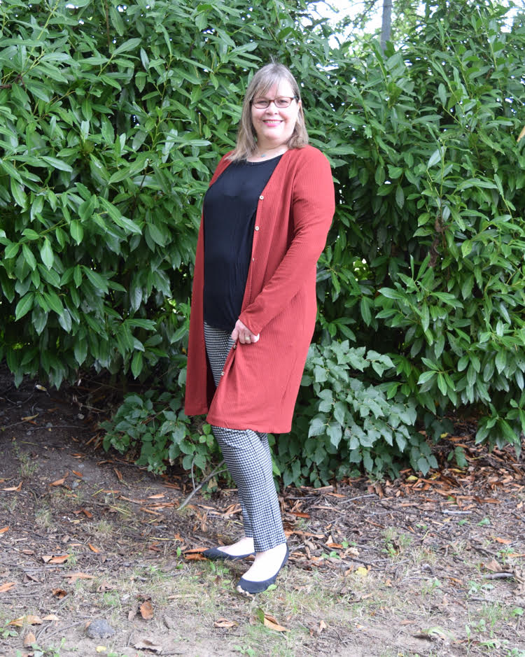 woman wearing a long orange cardigan, black tee, plaid pants and black shoes