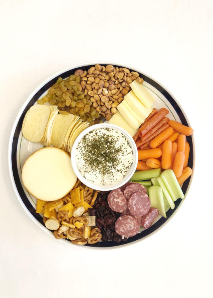 fall charcuterie board with cheeses, salami, celery and carrot sticks, potato chips and a snack mix