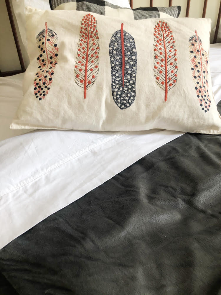 pretty pillow with a feather print over crisp white sheets and a plush gray weighted blanket