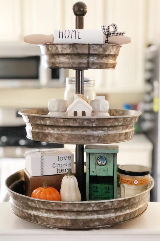 a three tiered galvanized tray filled with decorative salt and pepper shakers, a faux book stack and a mini white ceramic house.