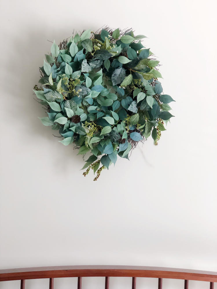 nearly natural faux wreath with green leaves and berries on a wall