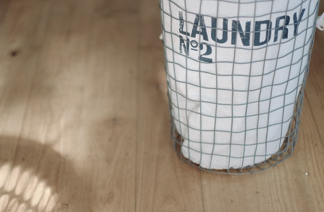 a wire laundry basket with a white laundry bag on a wood floor