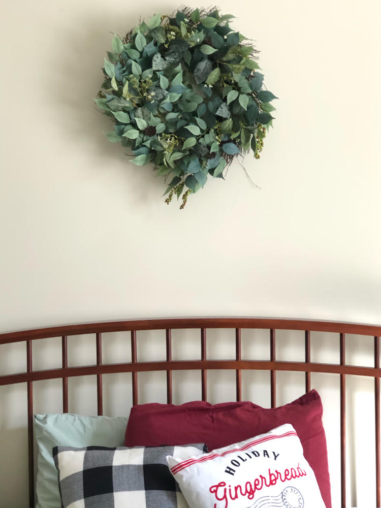 beautiful faux wreath of various green leaves and berries and mini brown vines over a bed with seasonal Christmas pillows