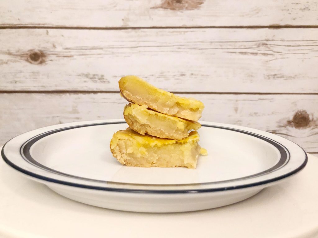 A stack of delicious homemade shortbread lemon bars on a white plate against a plank wall background