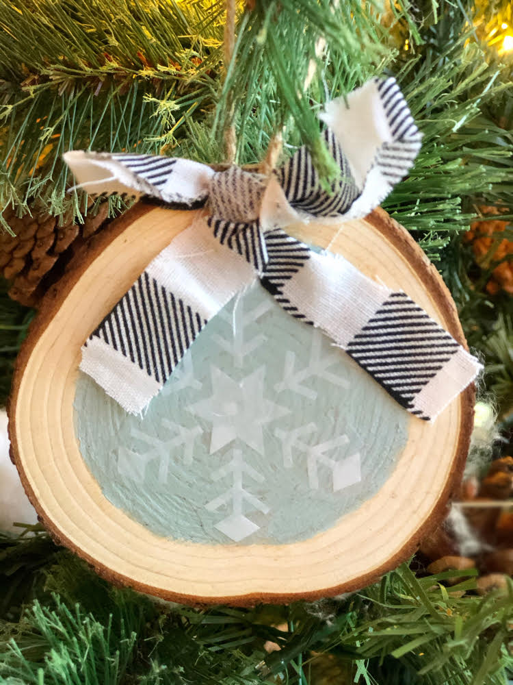 homemade snowflake wood slice ornament with a homemade buffalo plaid ribbon in a lit Christmas tree