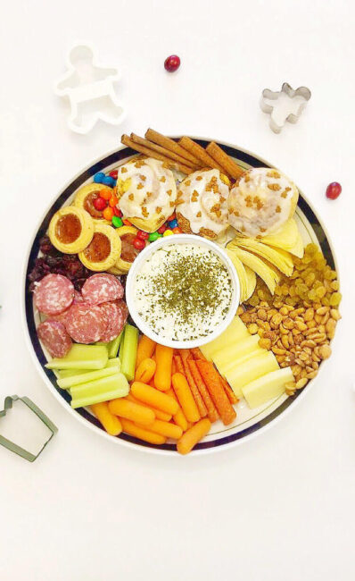 christmas charcuterie tray with cheeses, meats, veggies, dried fruits, cinnamon rolls and candy