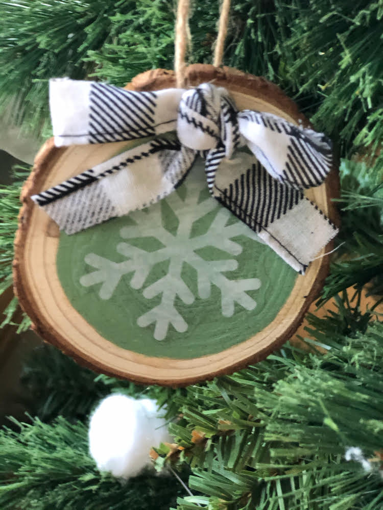 a homemade snowflake wood slice ornament with a black and white buffalo plaid ribbon