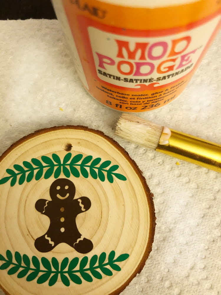 Applying Mod Podge over a vinyl design on a DIY wood slice ornament will help your design to last for as along as you need it