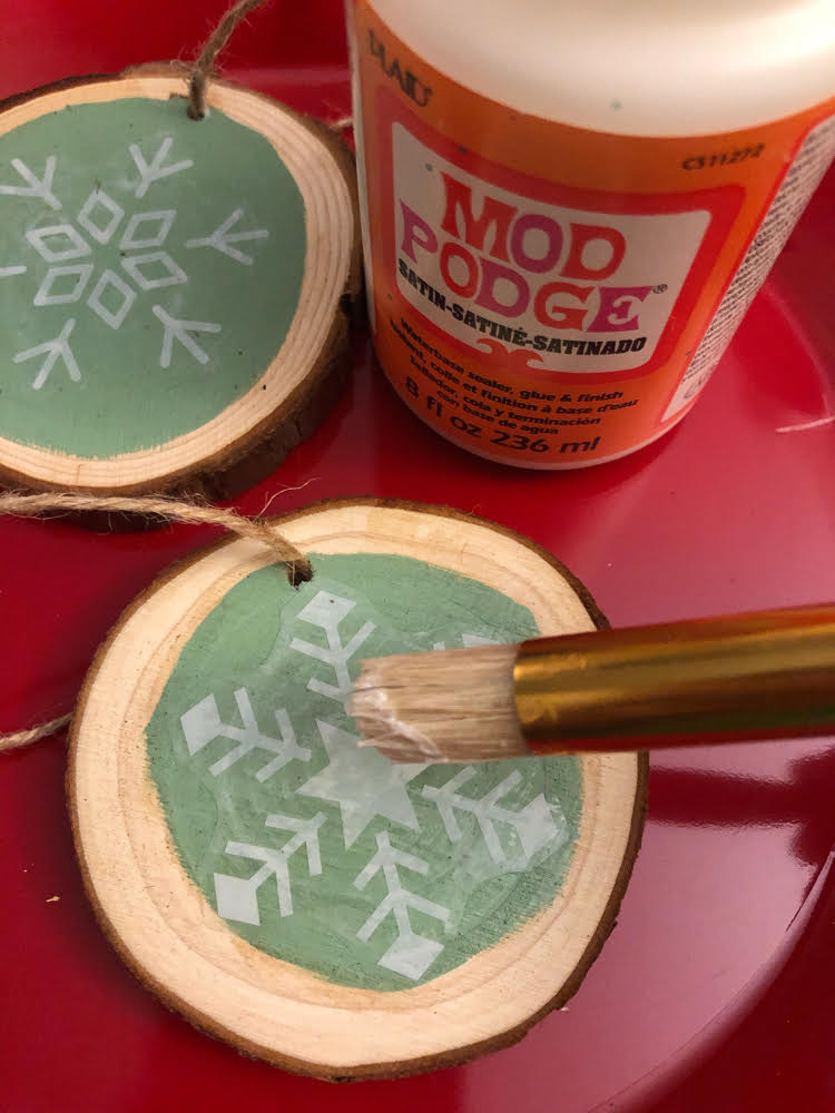 Using Mod Podge to decoupage a vinyl snowflake on a rustic wood slice ornament painted with DecoArt Chalky Finish paint in green