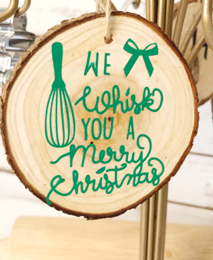 a homemade "We Whisk You a Merry Christmas" wood slice ornament on an ornament stand