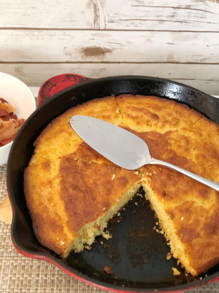 homemade cornbread in a cast iron skillet with a cake server