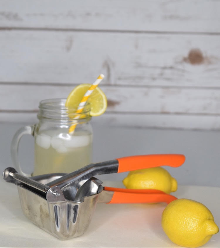 stainless steel citrus juicer, lemons and mason jar glass of lemonade