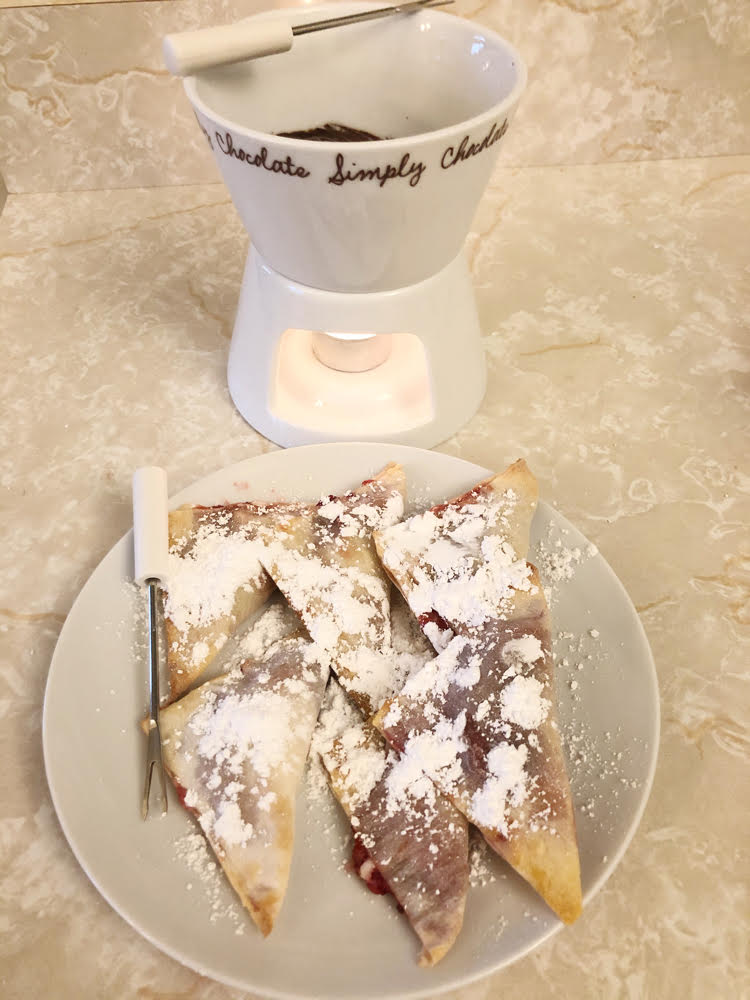 A chocolate fondue set with a plate of strawberry cream cheese air fried won tons.