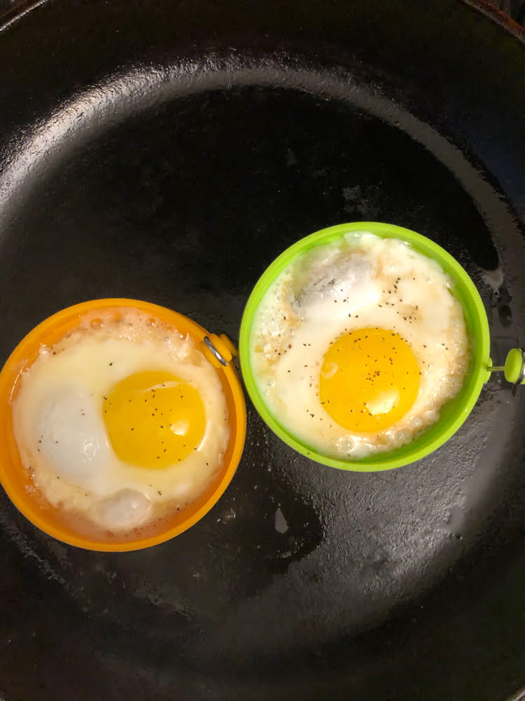 a yellow and a green silicone food grade egg and pancake ring and two fried eggs