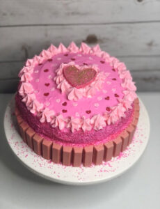 pretty homemade pink double layer cake topped with a pink candy heart and with pink KitKats on the sides