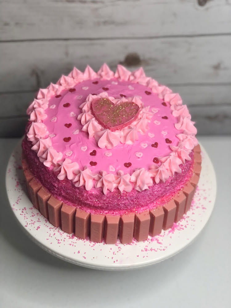 pretty homemade pink double layer cake topped with a pink candy heart and with pink KitKats on the sides