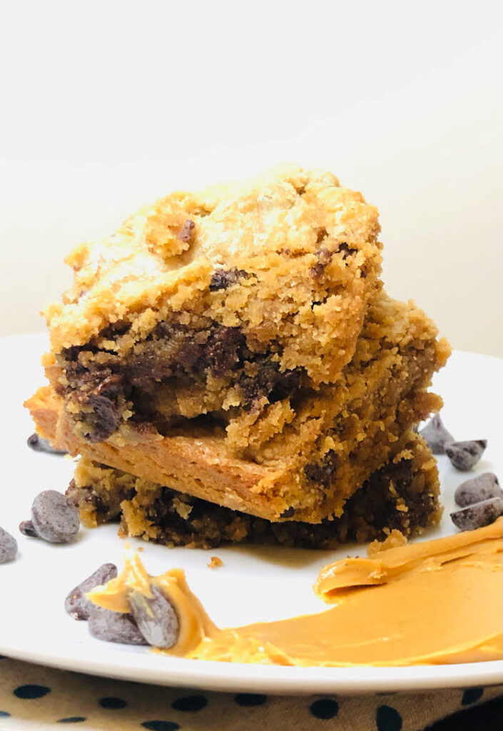 delicious and easy peanut butter chocolate chip bars on a plate with chocolate chips and a smear of peanut butter