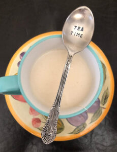 tea time engraved spoon placed across a mint green tea cup