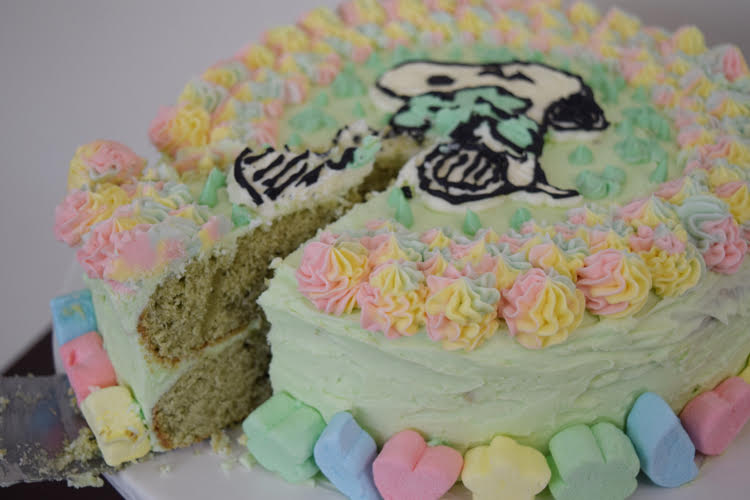 A green frosted cake with rainbow piped stars and a Snoopy and shamrock design on the top. The cake is lined with Lucky Charms marshmallows