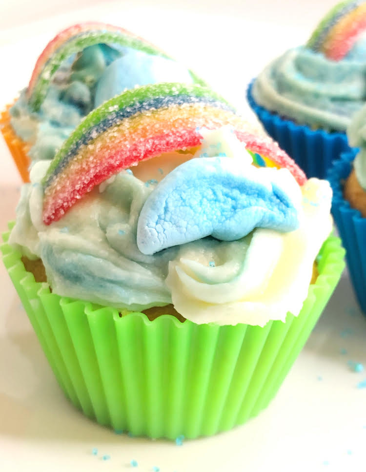 buttercream cupcake in silicone cupcake  cup, topped with Lucky Charm marshmallow clouds and a candy rainbow