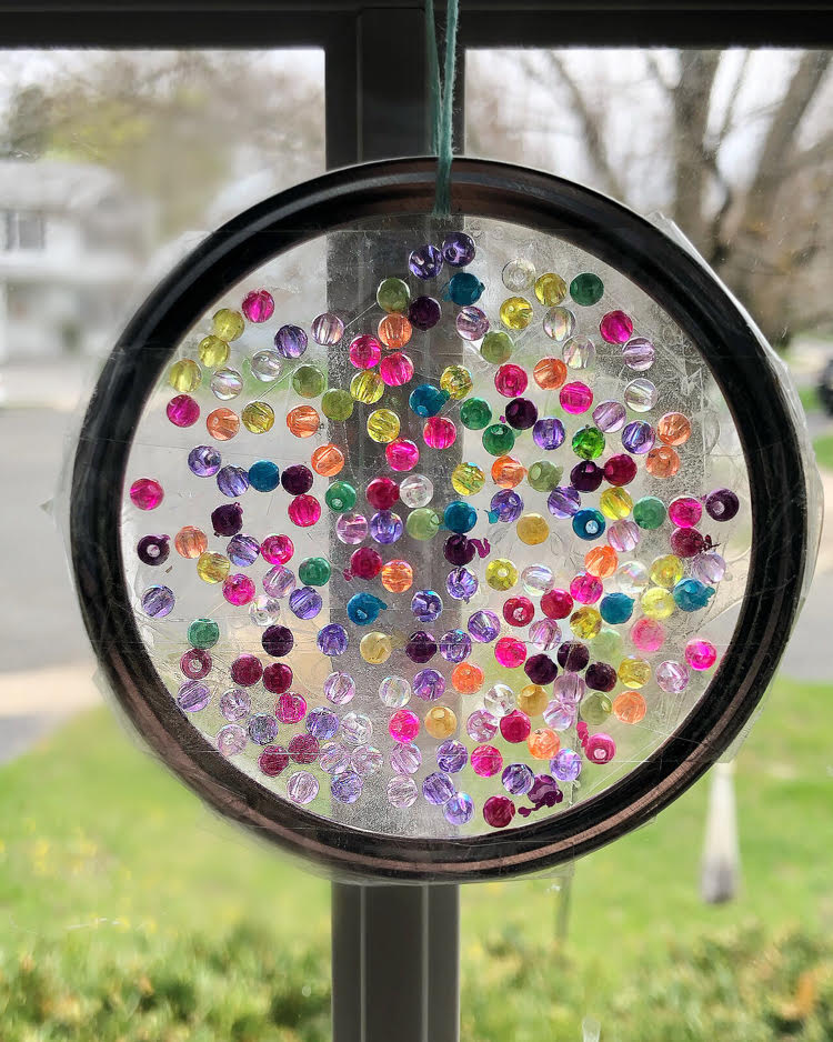 a DIY suncatcher made with a mason jar ring and small colorful iridescent beads and Duck tape