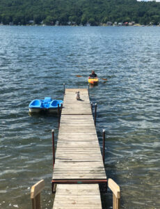 woman in kayak on lake and a dog on a dock