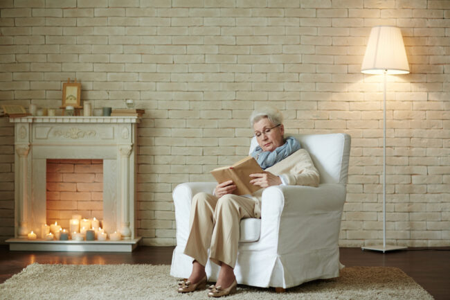 Woman reading in a cozy recliner by a candlelit fireplace.