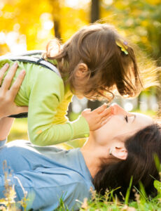 woman lying in the grass and holding her child in the air