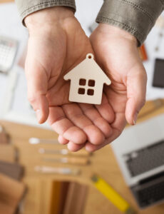 an individual holding a mini home in their hands over a keyboard and a written contract