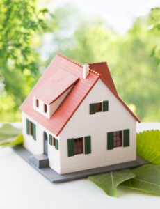 a cute model of a home placed on leaves with trees in the background