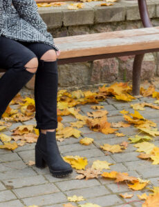 woman in ripped black leggings and a jacket sitting on a bench in the fall