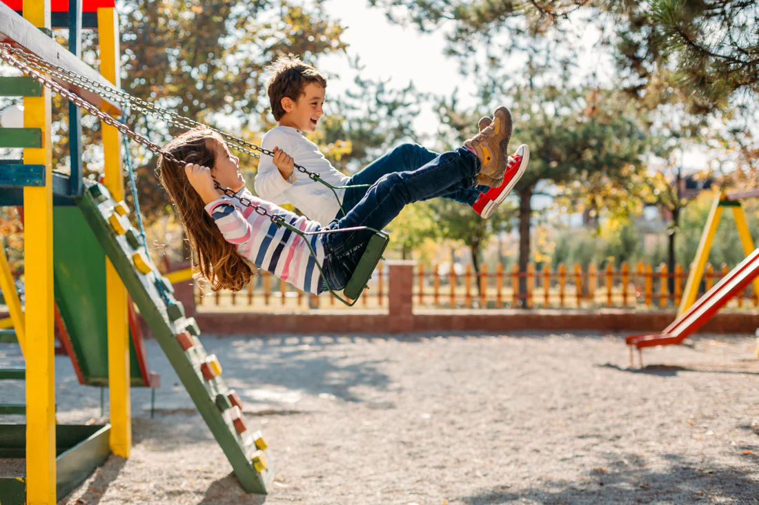 children enjoying an outdoor playground swing set