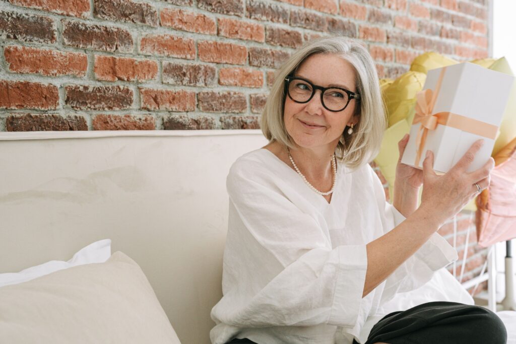 Senior woman in white blouse holding a gift box.